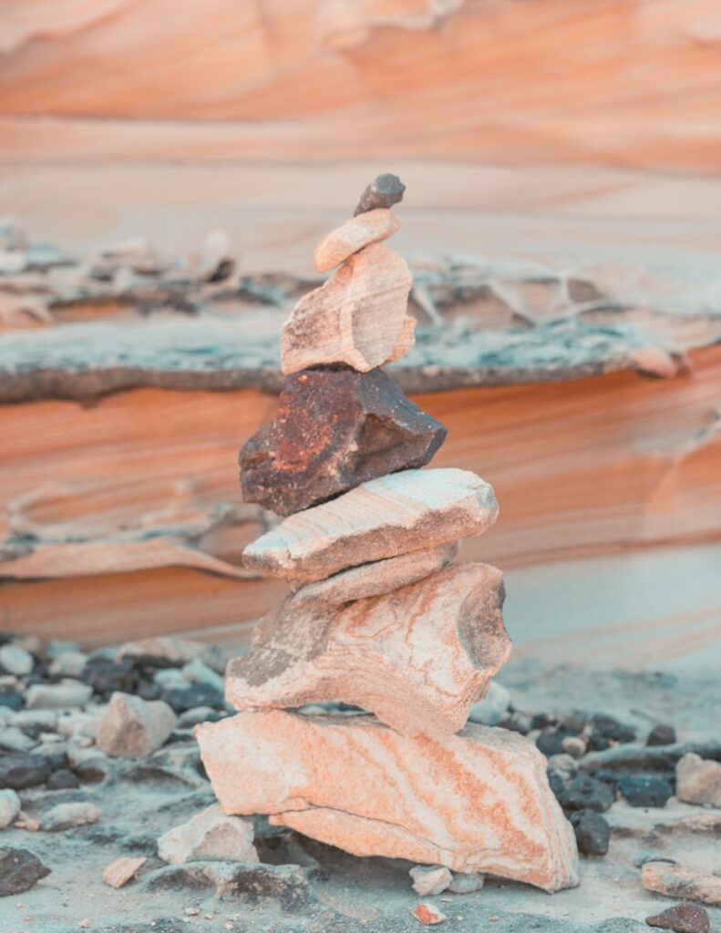 Pile of brownish-pink rocks stacked upon each other in the form of a cairn, against a rocky backdrop.